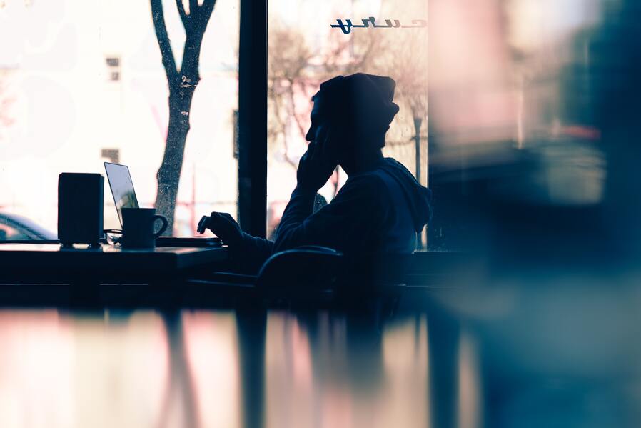 Silhouette of a person sitting in front of a laptop